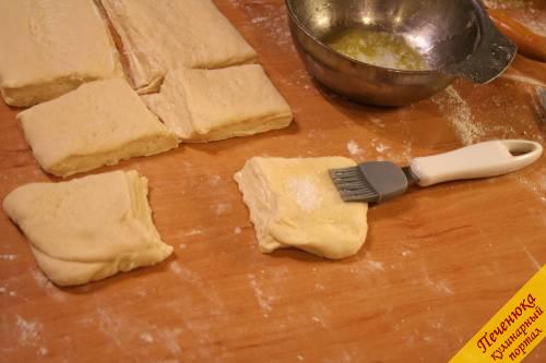 11) Формируем булочки из слоеного дрожжевого теста. Раскатываем готовое тесто в пласт толщиною 1 см. Разрезаем острым ножом на квадратики. Смазываем по середине растопленным сливочным маслом. Посыпаем сахаром. Соединяем все четыре уголка вместе. Защипываем их и приминаем в серединке. 