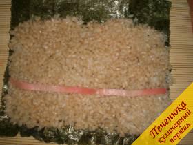 3) Условно разделить поверхность, устеленную рисом на 3 части. Между первой и второй частью будет выкладываться начинка. Сначала выложите полоску маринованного имбиря. 
